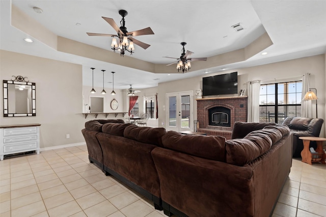 living area with light tile patterned flooring, visible vents, a raised ceiling, and a ceiling fan