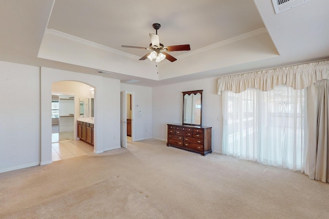 unfurnished bedroom featuring visible vents, ornamental molding, a tray ceiling, arched walkways, and light colored carpet