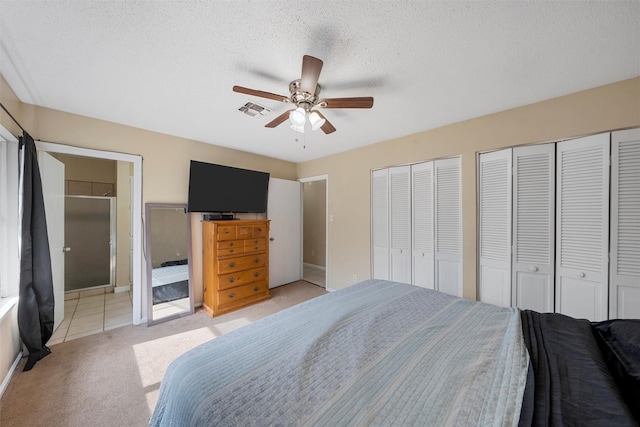 bedroom with visible vents, multiple closets, light carpet, a ceiling fan, and a textured ceiling