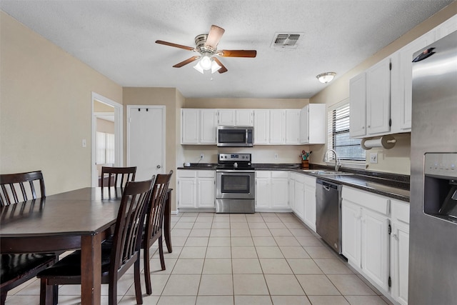 kitchen featuring light tile patterned flooring, a sink, ceiling fan, stainless steel appliances, and dark countertops