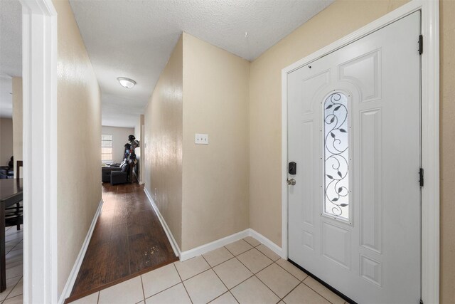 entryway with light tile patterned flooring, a textured ceiling, and baseboards