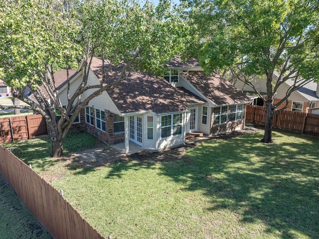 rear view of property with a lawn, roof with shingles, a fenced backyard, and a sunroom