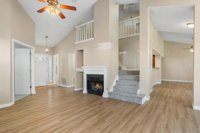 unfurnished living room with baseboards, light wood-style floors, a warm lit fireplace, and a ceiling fan