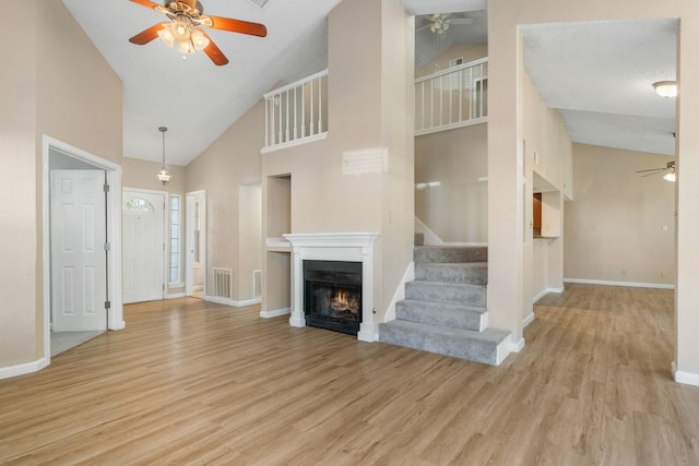 unfurnished living room with light wood-style flooring, baseboards, a warm lit fireplace, and ceiling fan