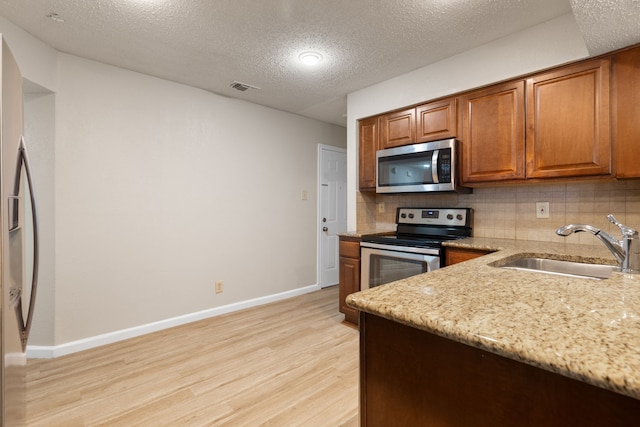 kitchen with visible vents, light wood-style flooring, a sink, decorative backsplash, and appliances with stainless steel finishes