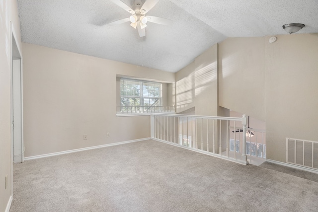 carpeted empty room featuring visible vents, a textured ceiling, baseboards, ceiling fan, and vaulted ceiling