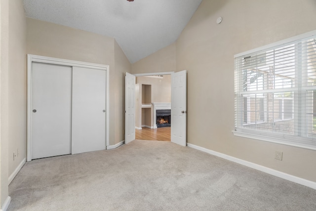 unfurnished bedroom with high vaulted ceiling, a closet, carpet floors, a lit fireplace, and baseboards
