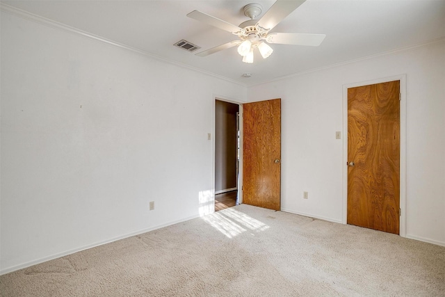 carpeted spare room featuring visible vents, baseboards, crown molding, and ceiling fan