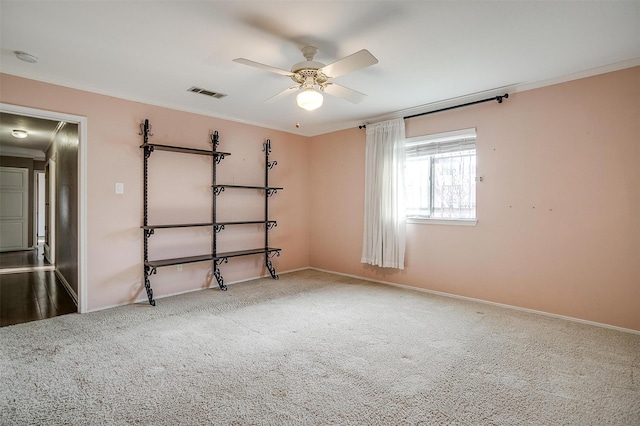 carpeted empty room with visible vents, baseboards, ceiling fan, and ornamental molding