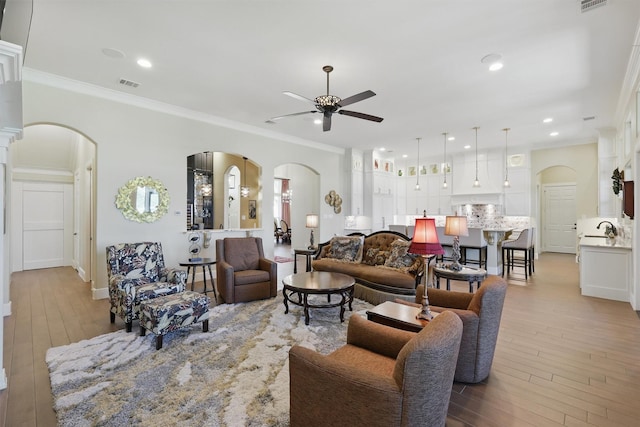 living area featuring arched walkways, visible vents, crown molding, and ceiling fan