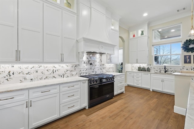 kitchen with visible vents, a sink, white cabinetry, range with two ovens, and custom exhaust hood