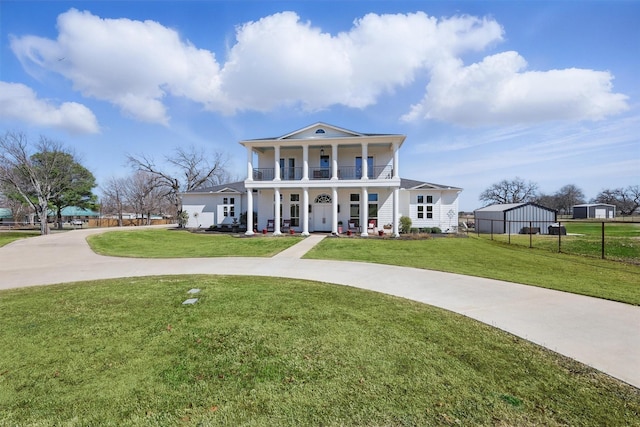 greek revival inspired property featuring a balcony, a porch, curved driveway, and a front yard