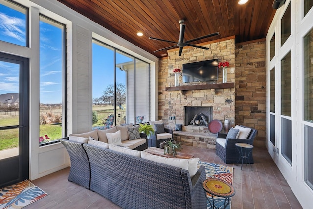 sunroom with wooden ceiling, an outdoor stone fireplace, and a ceiling fan