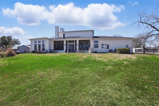 rear view of house featuring a lawn, a chimney, and a sunroom