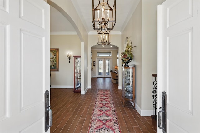 foyer entrance featuring baseboards, wood finish floors, arched walkways, crown molding, and a chandelier