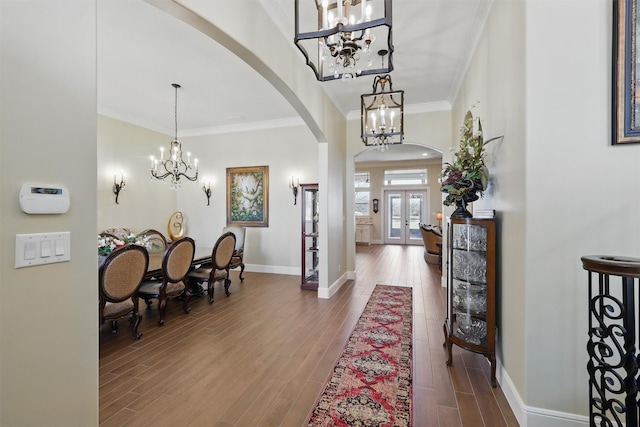 foyer with a notable chandelier, wood finished floors, arched walkways, and ornamental molding