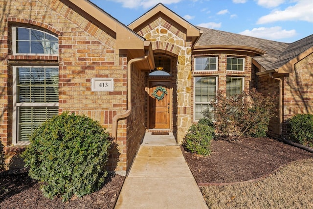 view of exterior entry with brick siding, stone siding, and roof with shingles