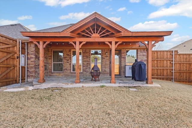 back of property with a lawn, fence, a shingled roof, brick siding, and a patio area