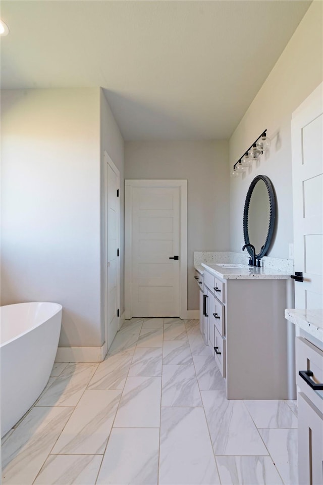 bathroom with baseboards, a freestanding bath, marble finish floor, and vanity