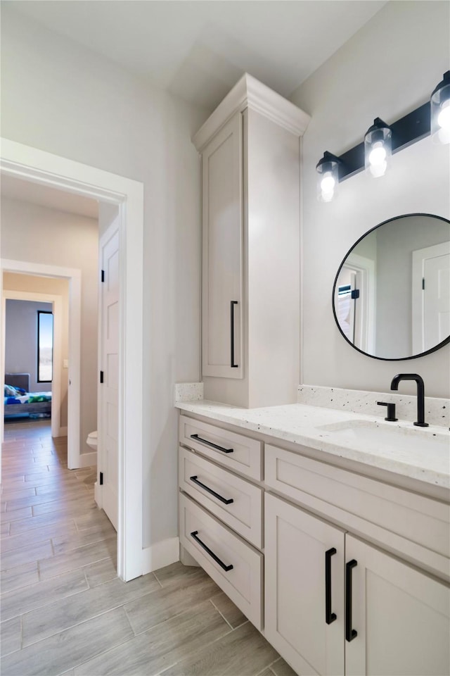 bathroom with wood finish floors, baseboards, toilet, and vanity