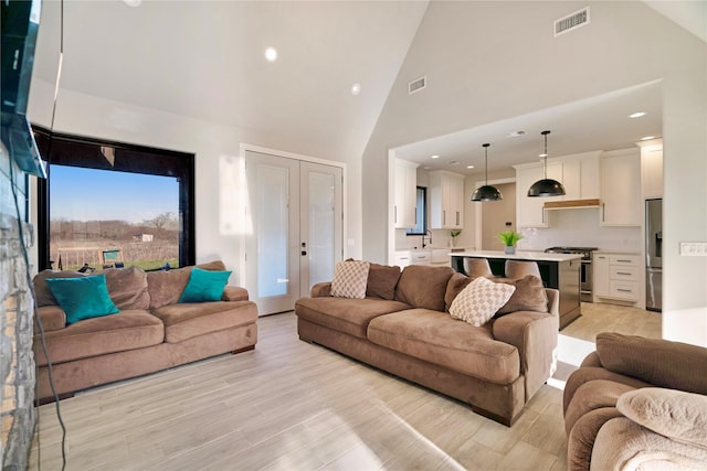 living room with recessed lighting, visible vents, light wood finished floors, and high vaulted ceiling