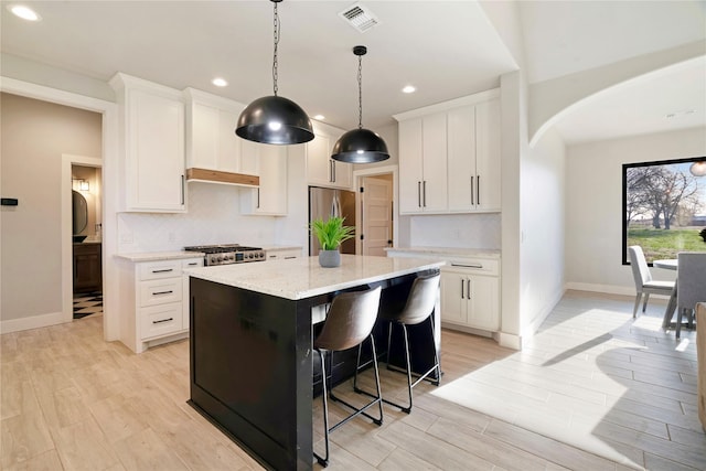 kitchen featuring visible vents, arched walkways, range, stainless steel fridge, and backsplash