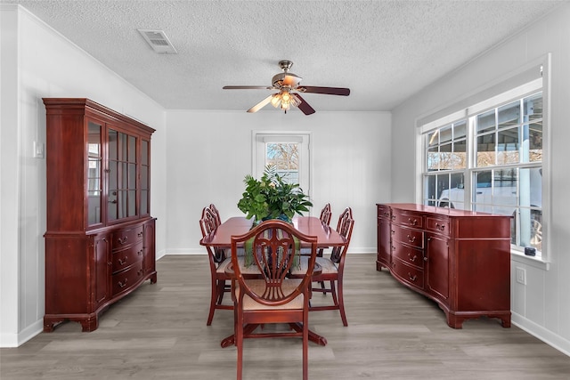 dining space featuring a ceiling fan, baseboards, visible vents, a textured ceiling, and light wood-type flooring