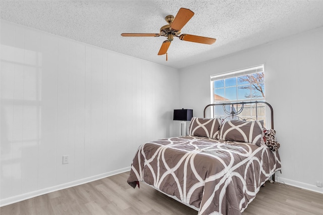 bedroom featuring light wood finished floors, baseboards, a textured ceiling, and ceiling fan