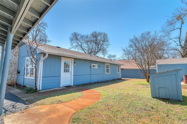 rear view of property featuring fence, a yard, a storage shed, roof with shingles, and an outdoor structure