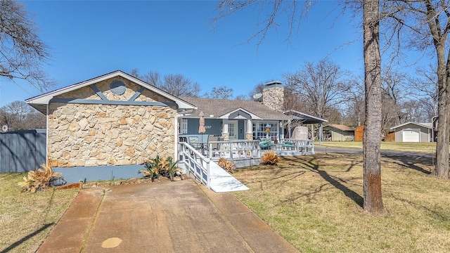 view of front of home with a front yard, roof with shingles, a porch, a chimney, and stone siding