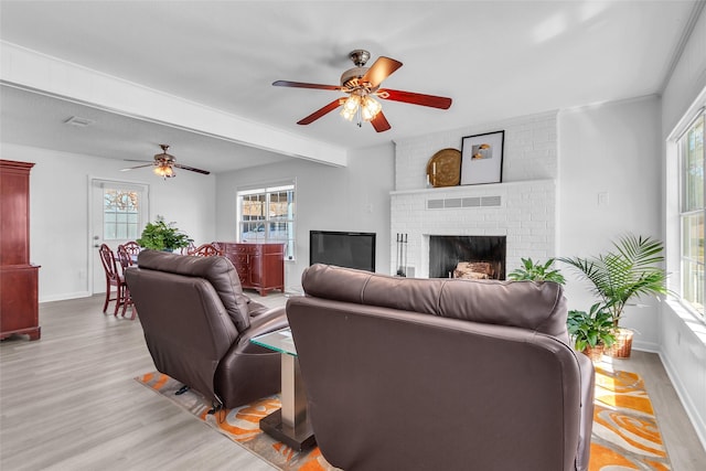 living area featuring a ceiling fan, visible vents, baseboards, a brick fireplace, and light wood-type flooring