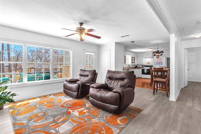 living room with light wood-type flooring, visible vents, a textured ceiling, baseboards, and ceiling fan