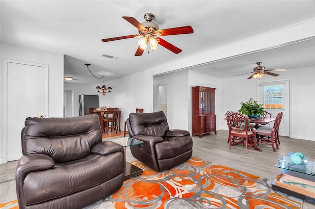 living room featuring visible vents, baseboards, light wood-style floors, and a ceiling fan