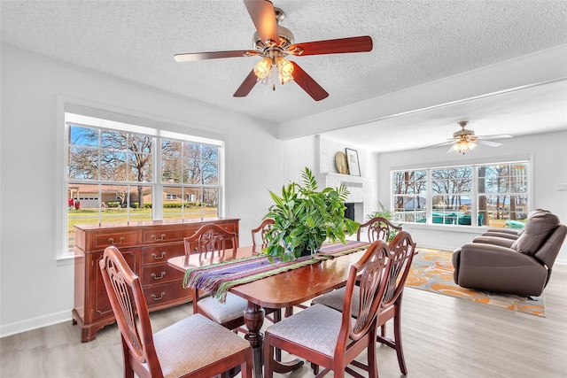 dining room featuring light wood finished floors, a brick fireplace, a textured ceiling, and a ceiling fan