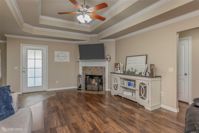 living room with wood finished floors, a fireplace, ornamental molding, ceiling fan, and a raised ceiling