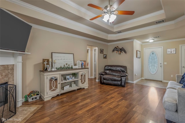 living area with a tray ceiling, wood finished floors, visible vents, and ceiling fan