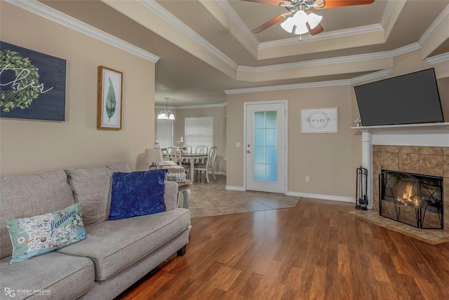 living area featuring a tray ceiling, wood finished floors, a tiled fireplace, and ceiling fan with notable chandelier