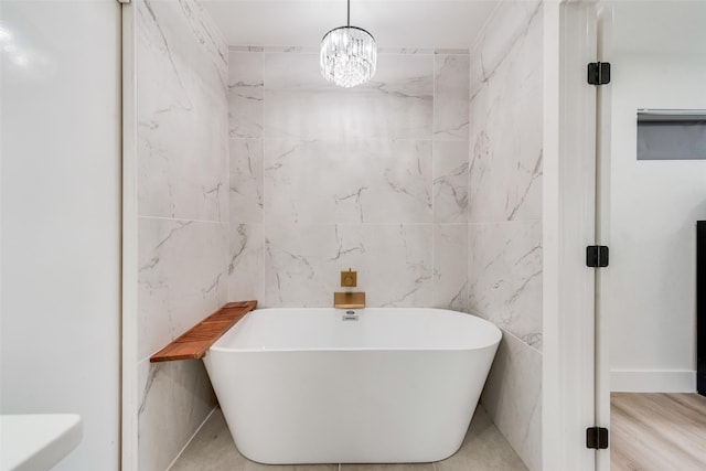 bathroom with a notable chandelier, a freestanding bath, and tile walls