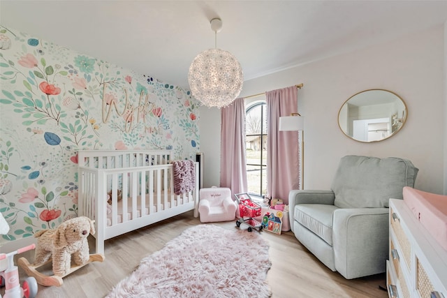 bedroom featuring a chandelier, wallpapered walls, a nursery area, and wood finished floors