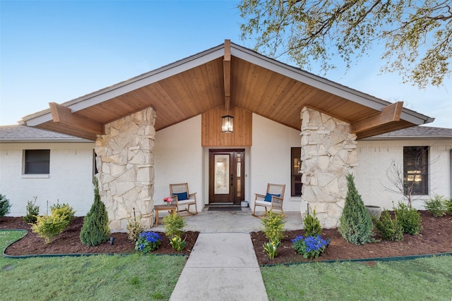 doorway to property featuring brick siding, stone siding, covered porch, and a shingled roof