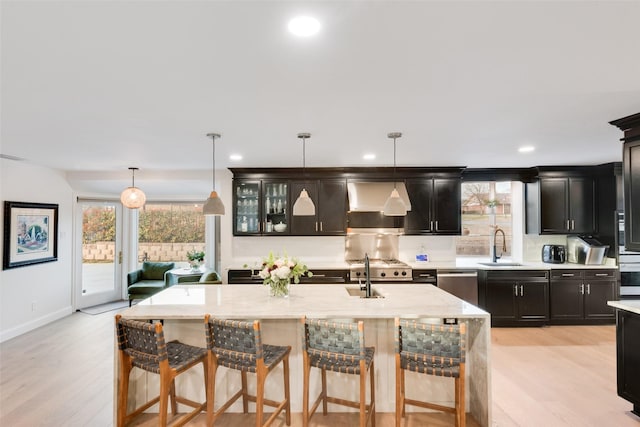 kitchen with wall chimney range hood, a breakfast bar, light wood-type flooring, appliances with stainless steel finishes, and a sink