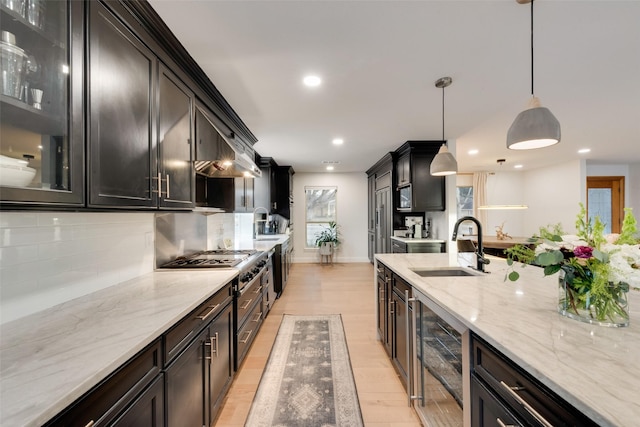 kitchen featuring beverage cooler, light wood finished floors, a sink, decorative backsplash, and glass insert cabinets