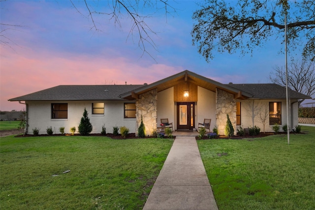 mid-century home featuring stone siding, a front yard, and roof with shingles