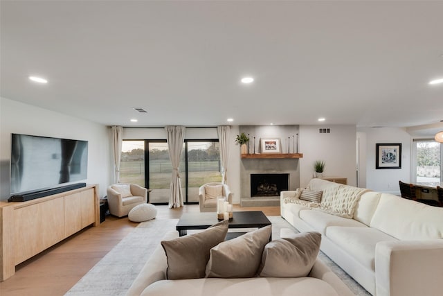 living area with visible vents, recessed lighting, light wood-type flooring, and a fireplace with raised hearth