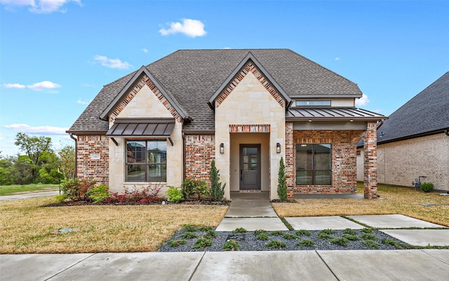 view of front facade featuring a standing seam roof, stone siding, a front yard, a shingled roof, and brick siding