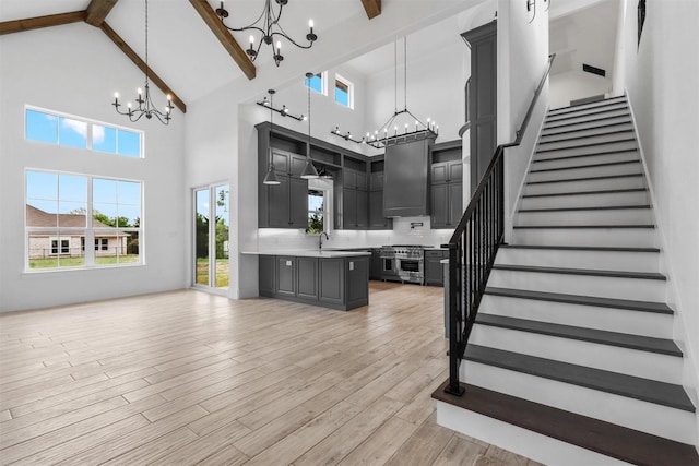 staircase with beam ceiling, high vaulted ceiling, wood finished floors, and a chandelier