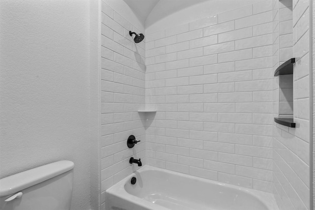 bathroom featuring toilet, a textured wall, and shower / washtub combination