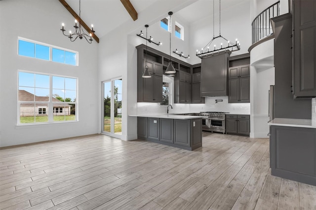 kitchen featuring beam ceiling, gray cabinets, light wood-style flooring, a notable chandelier, and wall chimney exhaust hood