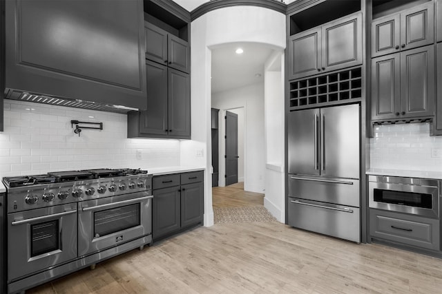 kitchen featuring tasteful backsplash, light countertops, light wood-style flooring, arched walkways, and high end appliances