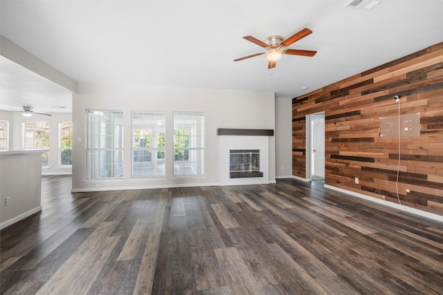 unfurnished living room with dark wood finished floors, wood walls, and ceiling fan